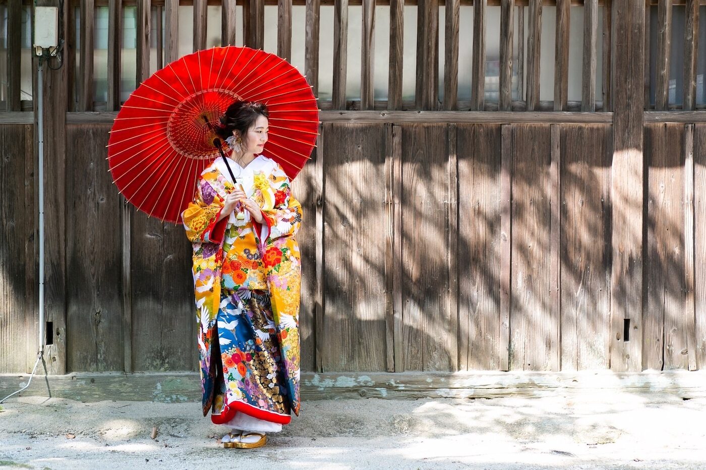 色打掛に赤い和傘を合わせた花嫁。古い板壁の前で