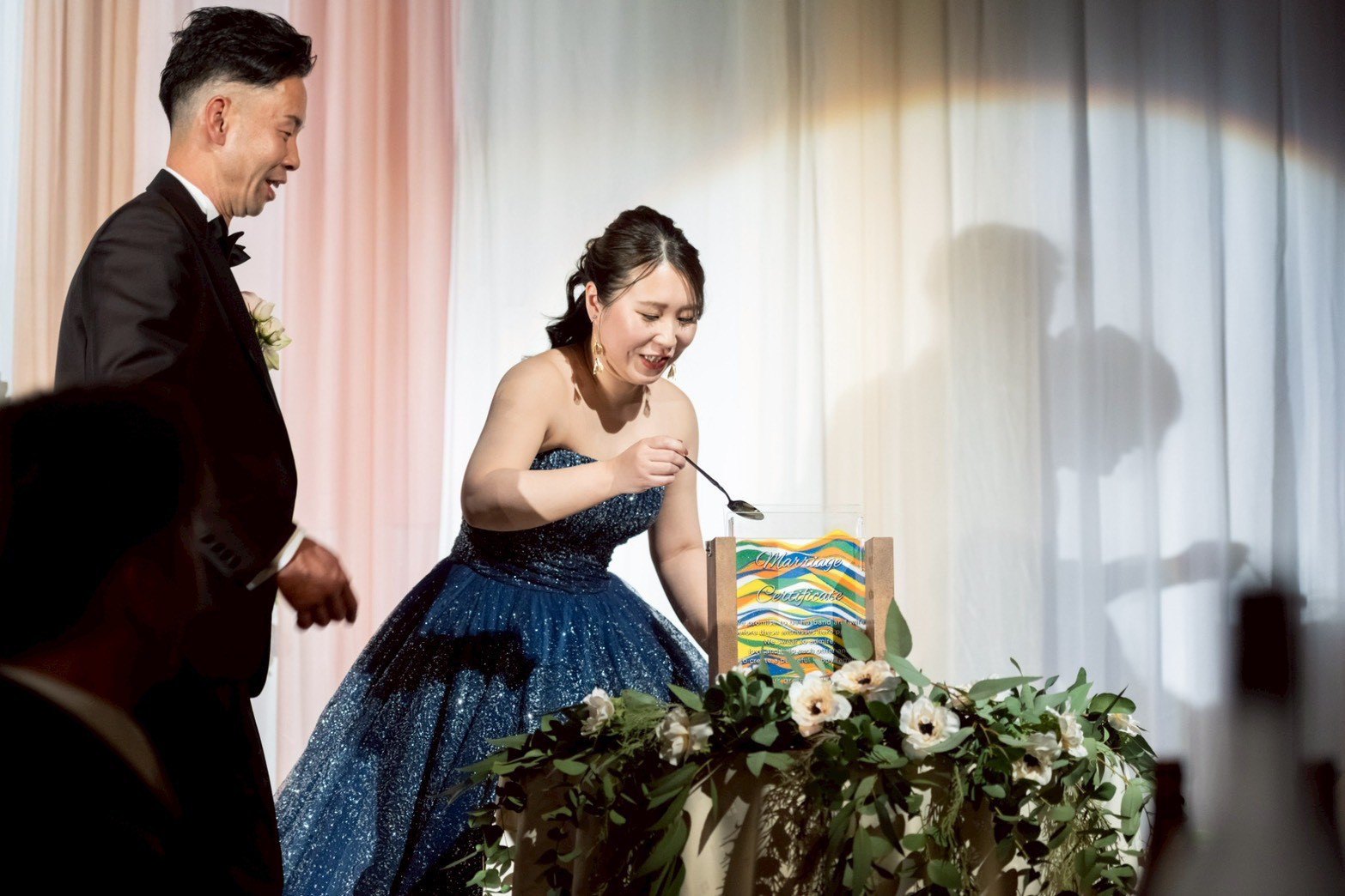ネイビーのカラードレスの新婦がスプーンで色砂を注いでいる